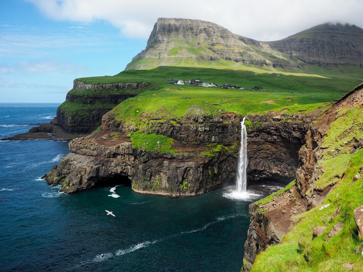In the photo, Mulafossur Falls falls from a cliff into the ocean. Mulafossur Waterfall